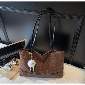 Dettaglio della borsa tote leopardata con manici neri e ciondolo in peluche bianco sulla scrivania