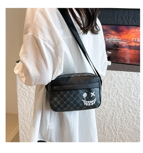 Detail of woven checkerboard crossbody bag with white graffiti face and nylon strap