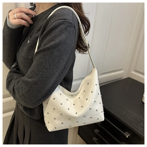 On-shoulder view of a white hobo bag with silver rivets and glossy patent finish