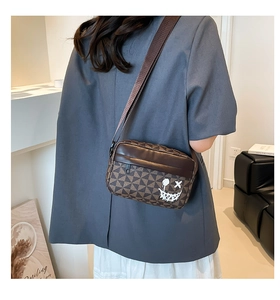 Detail of crossbody bag with brown geometric pattern and white graffiti smiley face print