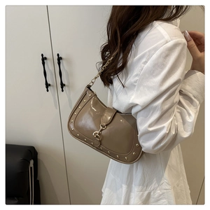 Close-up of khaki patent leather crescent bag with gold studs and chain strap detail