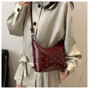 Detailed view of silver rivets on dark red faux leather shoulder bag with smooth texture