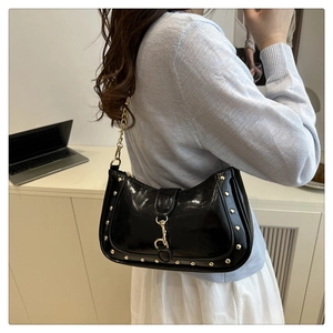 Detail of black glossy crescent bag with gold studs and metal chain shoulder strap