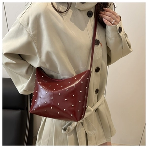 Detail of dark red glossy leather crossbody bag featuring silver metallic studs and slim strap