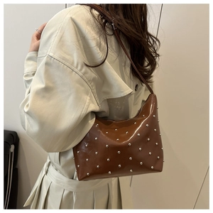 Detail of a brown glossy leather hobo bag with silver rivets worn over a beige coat