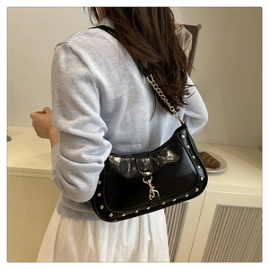Detail view of black glossy crescent bag with gold rivets and chain strap on a model