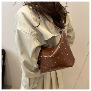 Close-up of glossy brown leather shoulder bag with silver rivet studs and a slim strap