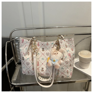 Close-up of white floral tote bag with pink heart embroidery, pearls, and bear charm