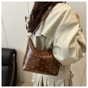 Close-up of brown shiny PU leather bucket bag with silver metal rivets and adjustable strap
