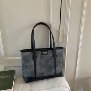 Detail of grey textured tote bag with black leather straps and brand label