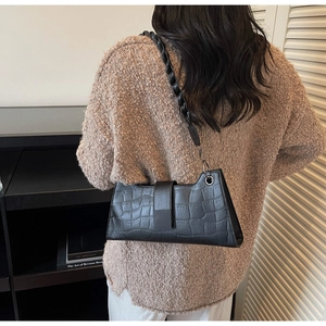 Detailed view of black crocodile pattern baguette bag with woven strap and metal eyelets