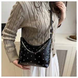Detail of a black glossy leather bucket bag with silver rivet studs worn with a knit cardigan