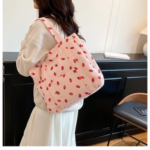 Detail of pink corduroy tote bag with strawberry print worn by model in home setting
