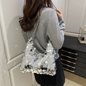 Silver sequin crescent shoulder bag with fish-scale texture worn by a model in interior