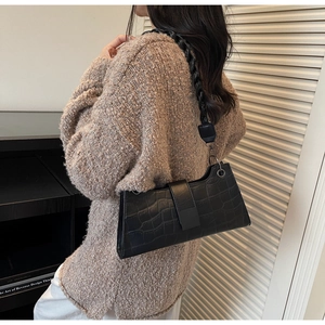 Close-up of black crocodile texture baguette bag with thick woven shoulder strap and flap