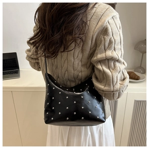 Close-up of a black leather hobo bag with silver studs worn by a model in a cozy room