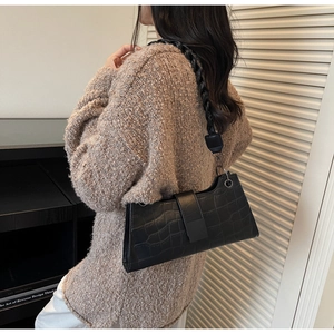 Detail of black crocodile pattern faux leather baguette bag with woven strap and metal ring