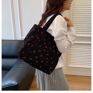 Detail of black corduroy tote bag with red strawberry print worn by a model