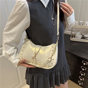White crescent crossbody bag with gold studs and chain strap shown in an indoor setting