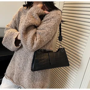 Detail of black crocodile texture baguette bag with thick woven shoulder strap on knit sweater