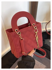 Dettaglio borsa trapuntata rossa con manico semicircolare, catena dorata e ciondolo