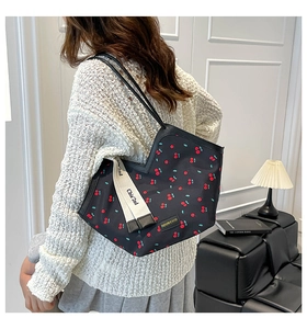 Detail of cherry print tote bag with dual straps and brand label on a black nylon base
