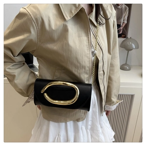 Close-up of black crossbody bag with large gold oval buckle and fine chain strap detail