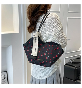 Detailed view of black tote bag featuring red cherry print and logo strap on model shoulder