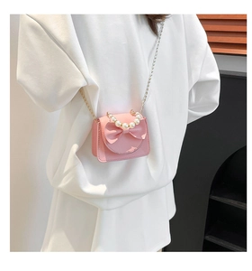 Pink mini crossbody bag with a large bow, pearl handle, and metal chain on a model