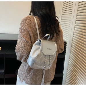 Silver mini backpack with chain strap and cartoon print worn by a model in a modern room