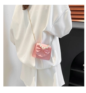 Detail view of pink crossbody bag with 3D bow, pearl handle and gold chain strap