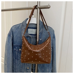 Detail of brown glossy leather bag featuring silver metal rivets and adjustable strap