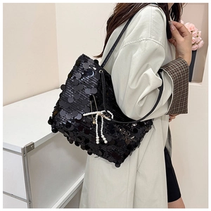 Detail of black sequin shoulder bag featuring a white pearl bow charm and slim strap