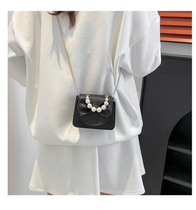 Close-up of black mini crossbody bag featuring a large bow and pearl handle detail