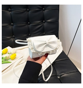 Close-up of white mini shoulder bag featuring a 3D bow and delicate lace edge detailing