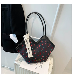 Detail of black cherry print tote bag with woven strap on a white suitcase