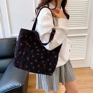 Black corduroy tote bag with red strawberry pattern and shoulder straps on a sofa