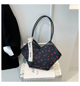 Detail of a chic black tote bag with cherry prints and branded strap on a suitcase