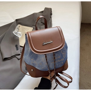Detail of the blue denim and brown leather backpack with chain drawstring and metal logo