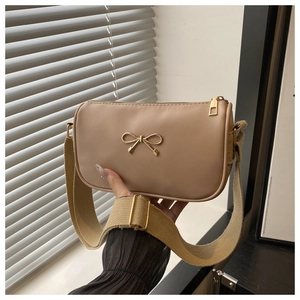 Detail of beige faux leather handbag featuring a gold bow accent and wide woven strap