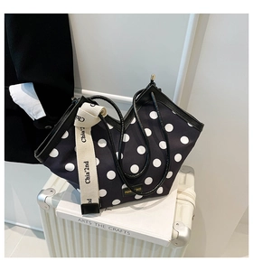 Detail of polka dot tote bag with wide logo strap on white book and silver suitcase