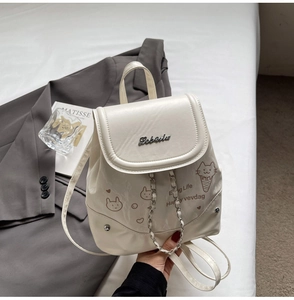 Detail of cream PU backpack featuring metal logo, cartoon prints and silver chain accents