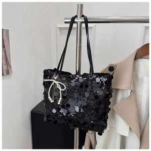 Detail shot of black sequin tote bag with a white pearl bow charm and long shoulder straps