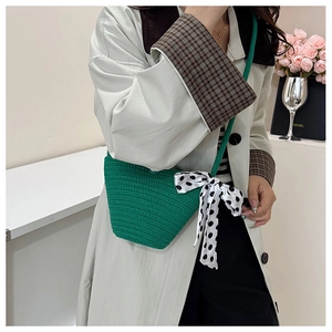 Détail du sac seau vert tressé avec ruban à pois porté sur un trench-coat beige