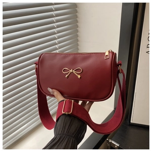 Detailed shot of burgundy crossbody bag with gold bow clasp and wide woven shoulder strap