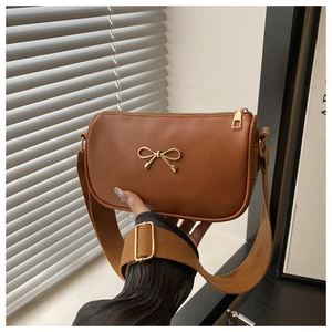 Detail of caramel brown crossbody bag featuring golden bow buckle and canvas strap