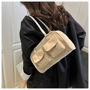 Detail of beige canvas baguette bag featuring dual front pockets and white piping accents