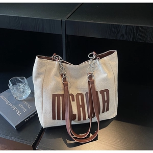 Detail of canvas tote bag with brown leather letters and metal chain shoulder strap