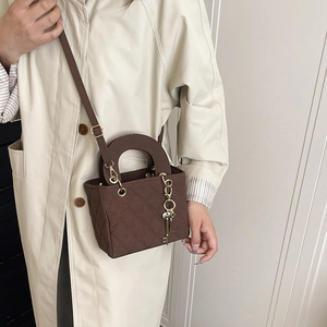 Borsa a mano trapuntata marrone con ciondolo a chiave dorata su trench beige