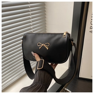 Detail of black leather crossbody bag with golden bow emblem and adjustable wide strap